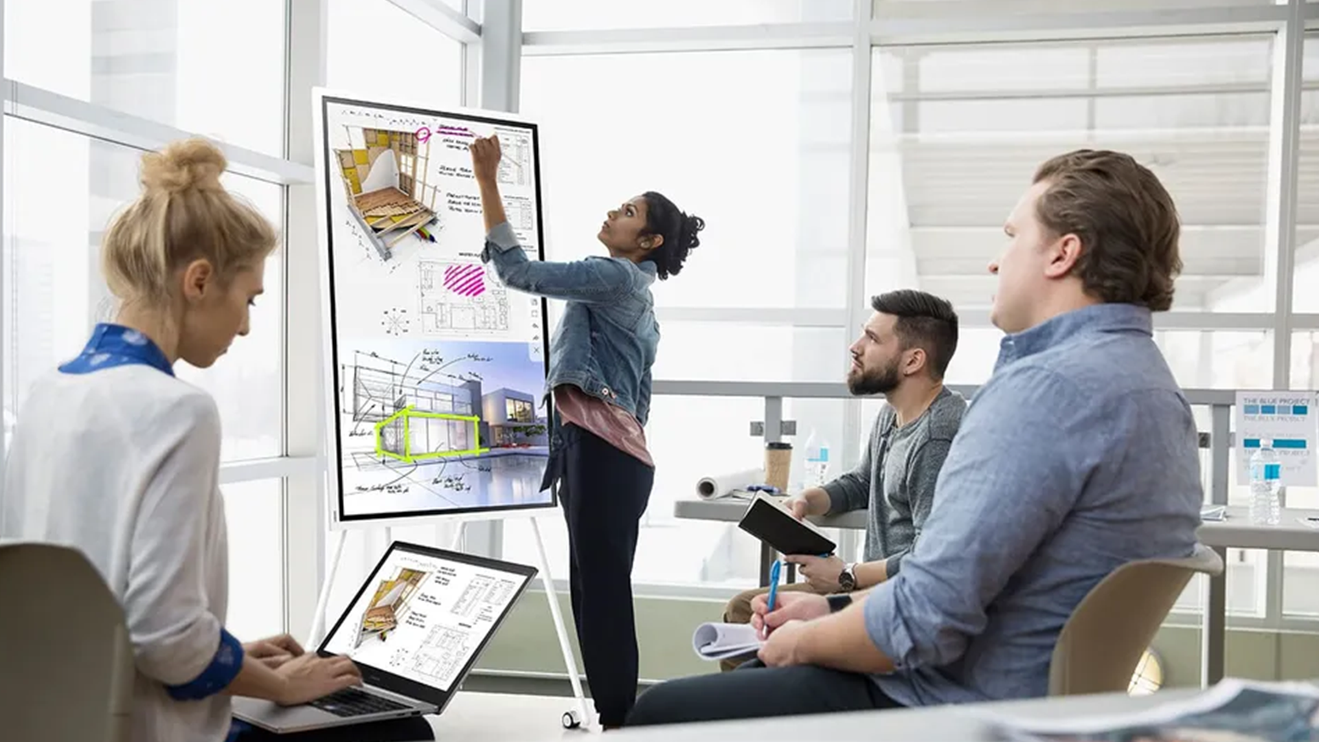 Eine Architektin schreibt während eines Meetings mit einem Stift auf das Samsung Flip Pro, während ihre Kollegen aufmerksam zuschauen – fördert interaktive Präsentationen und kollaborative Teamarbeit.